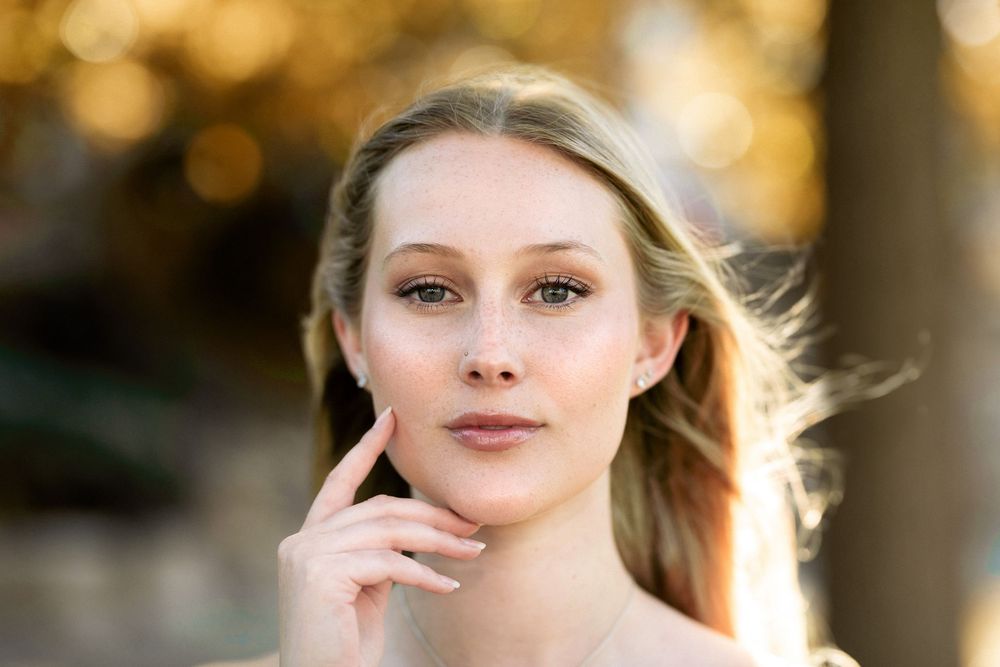 Portrait with soft natural lighting and gentle pose against blurred autumn background.