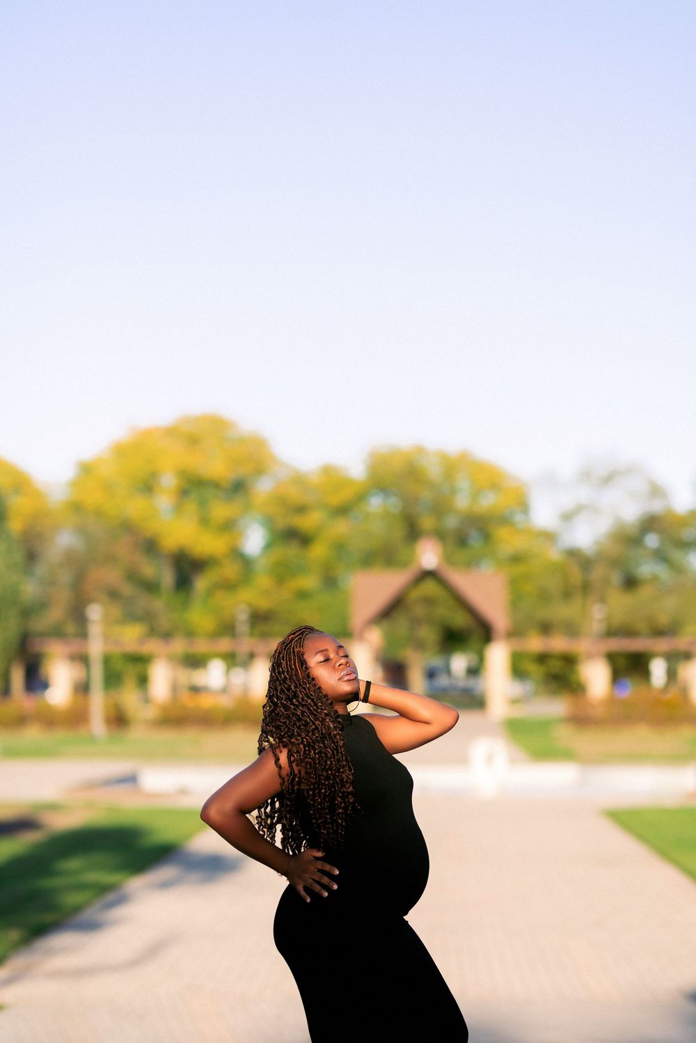 Artistic maternity silhouette against bright blue sky and trees.