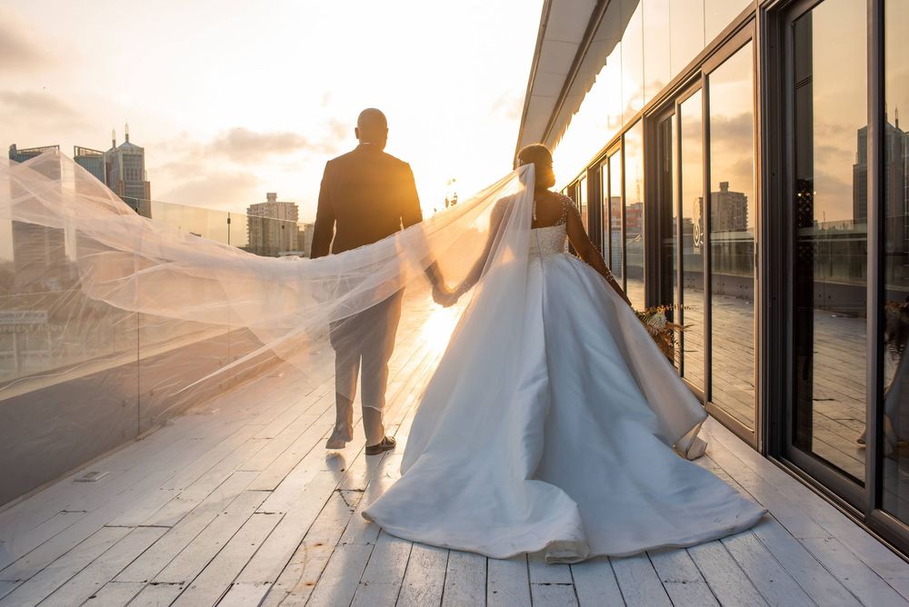 Silhouette of newlyweds walking on rooftop during sunset with flowing wedding dress.