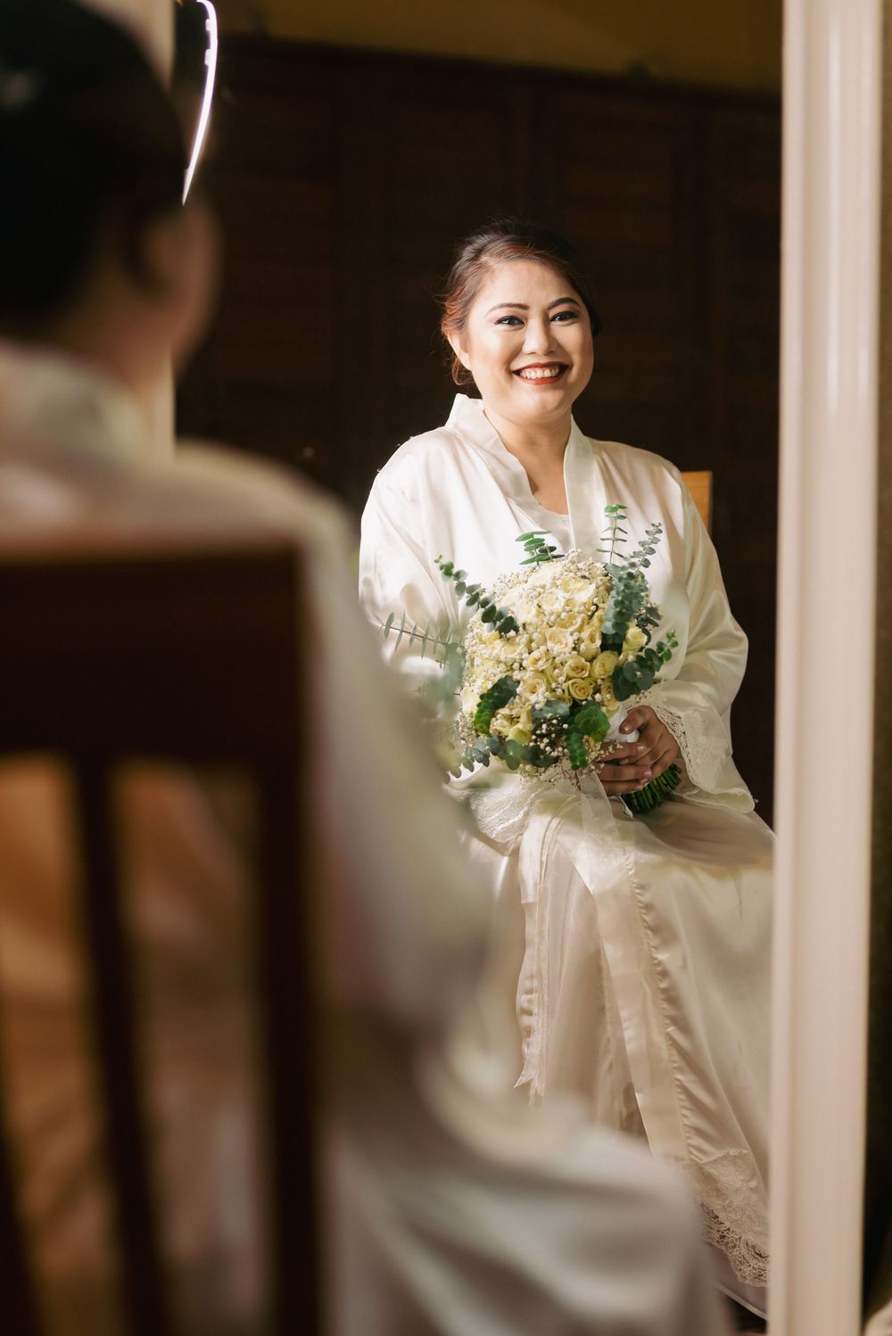 Person in white holding a bouquet of yellow and green flowers preparing for the wedding day.