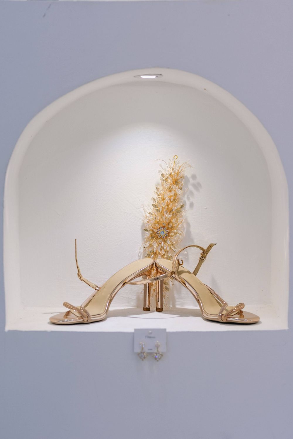 Wedding accessories display featuring gold heels and floral decor in an arched alcove.