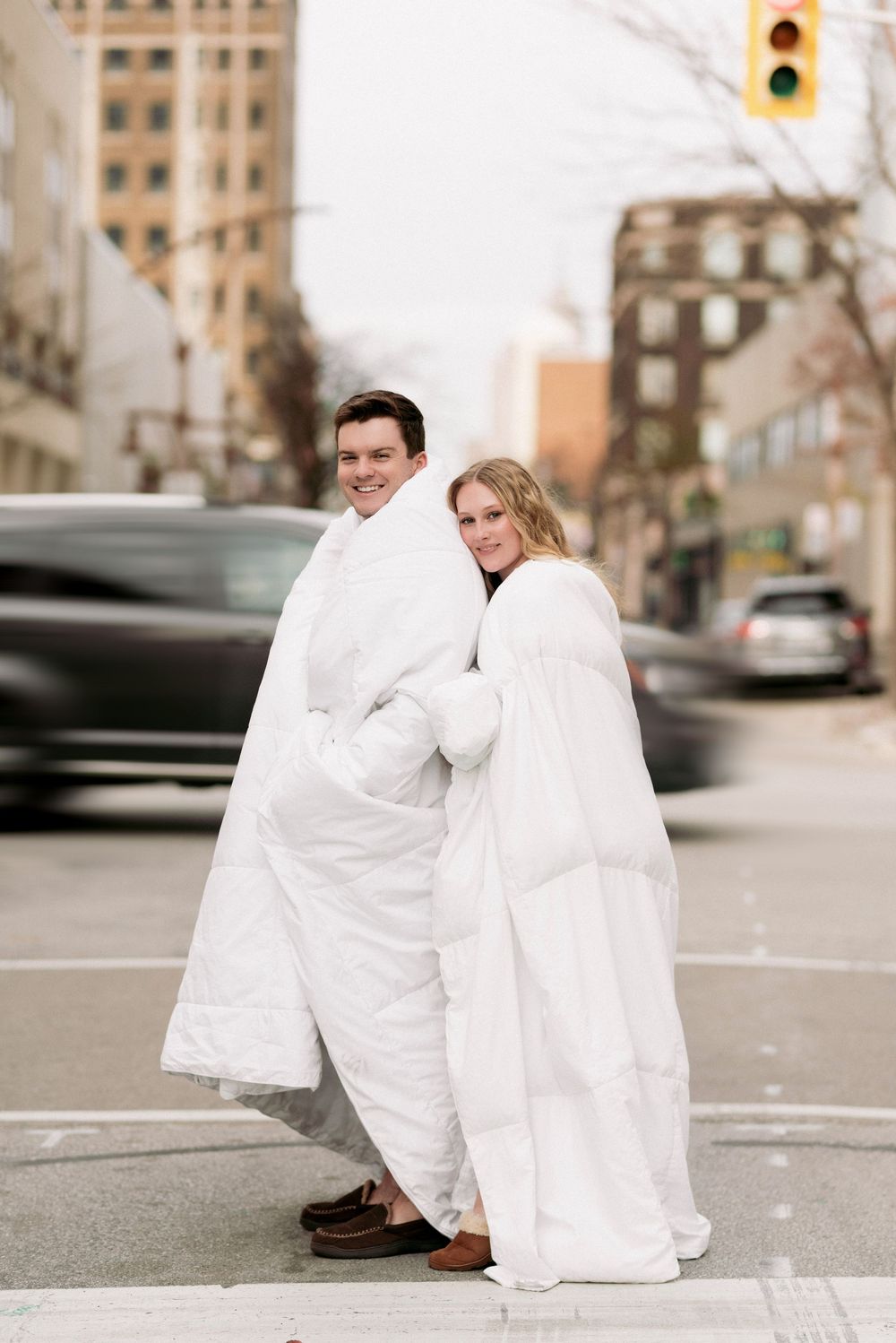 Couple wrapped in white blankets standing together on a city street corner.