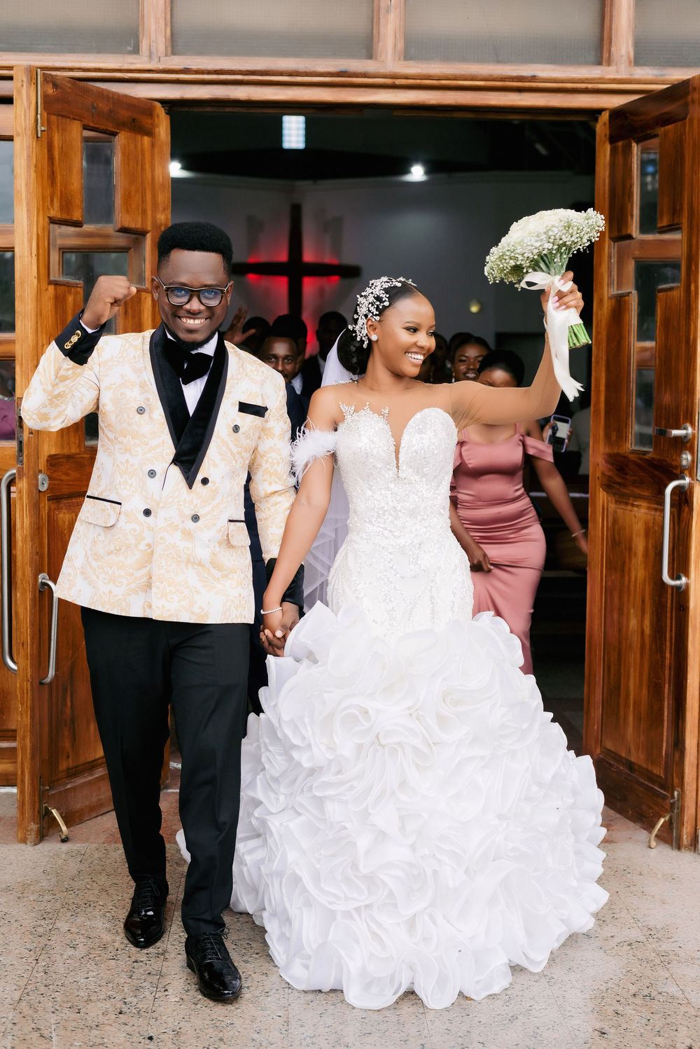 A newlywed couple exits through wooden church doors in elegant wedding attire.