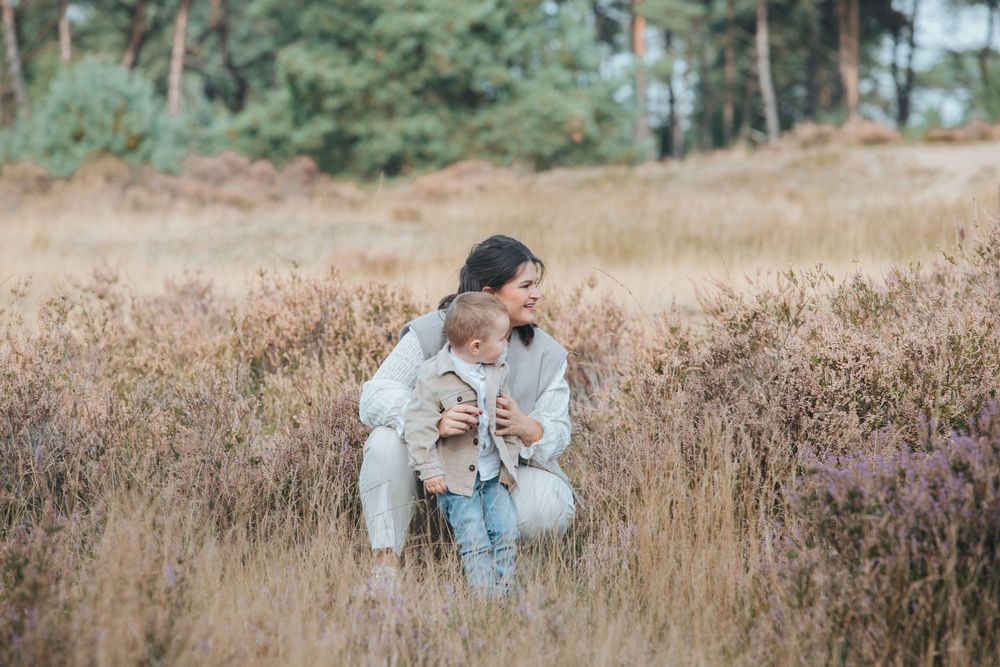 A person in denim sits on a fallen tree in a golden autumn field with wildflowers at sunset.