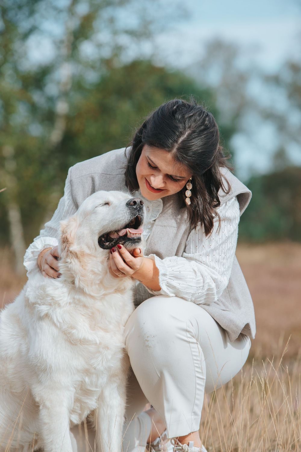 A white fluffy dog and their owner share affectionate moments in a field during an autumn photoshoot.