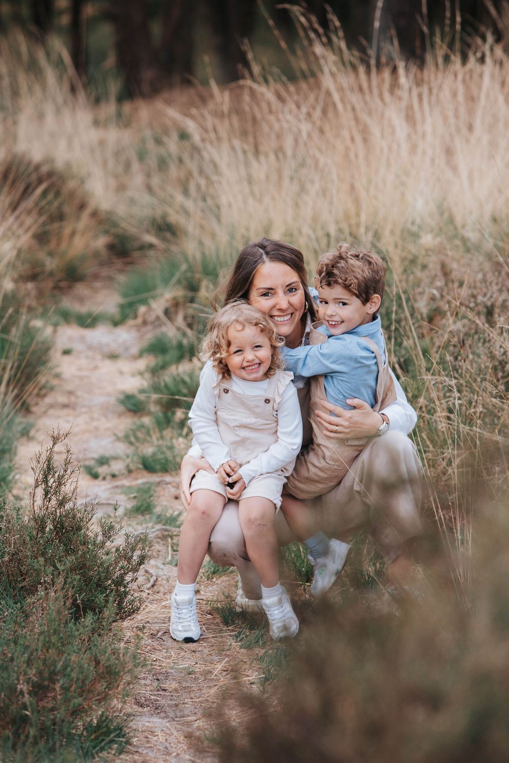 A family poses together on a nature trail surrounded by tall grass on a sunny afternoon.