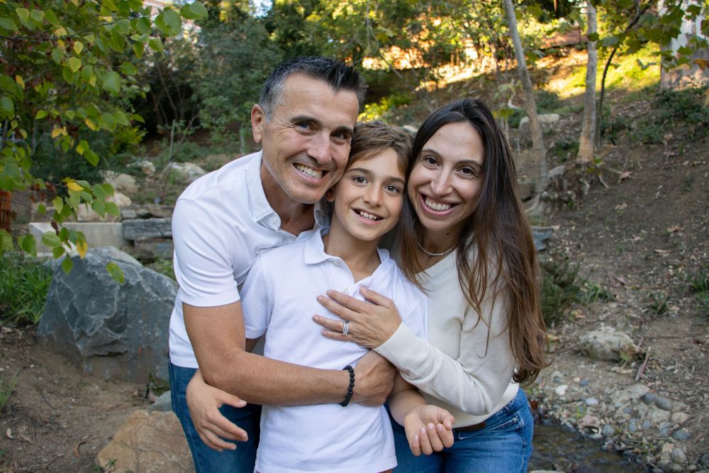Family members sharing warm embraces in a natural outdoor setting with trees.