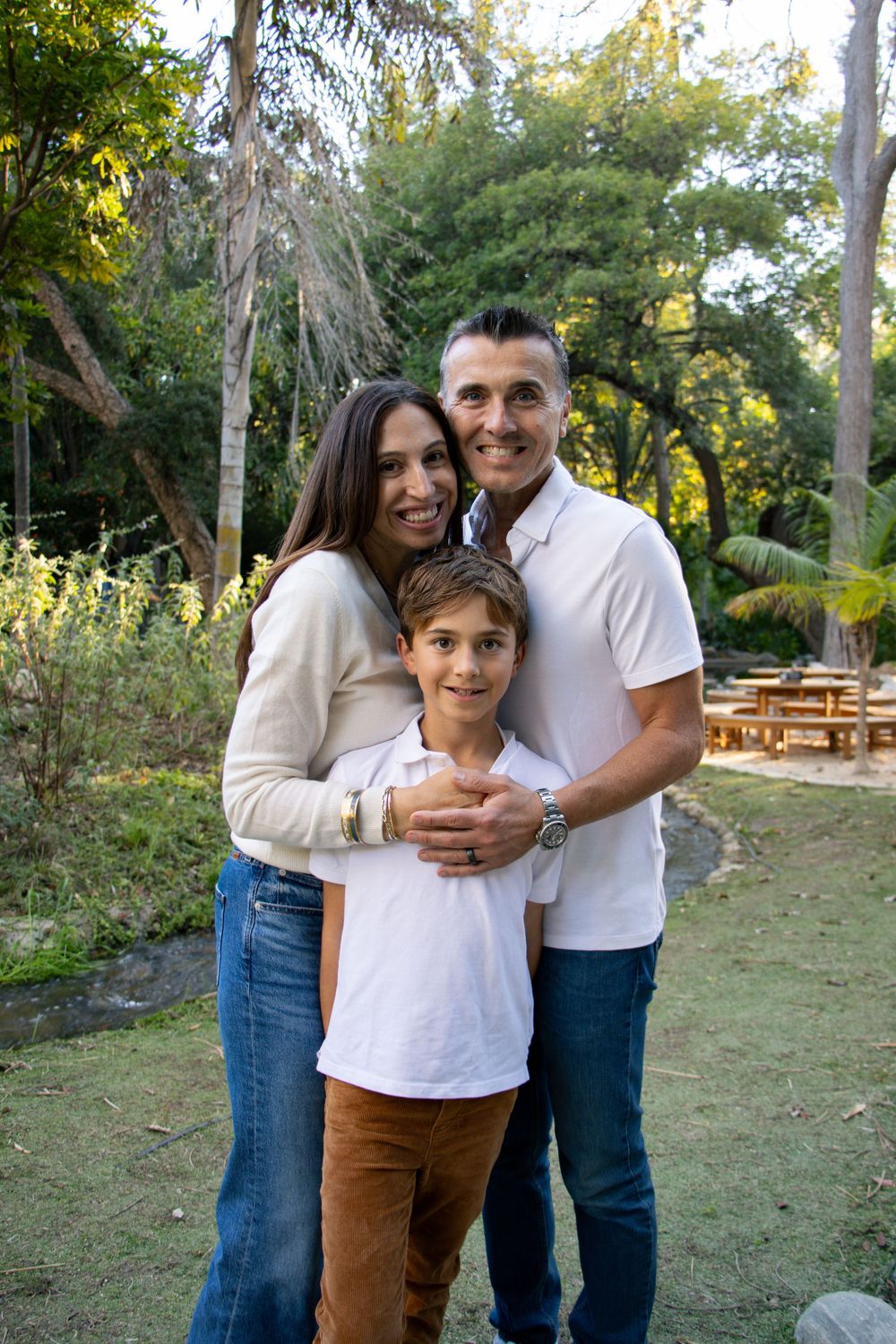 Family group sharing hugs and smiles in a garden setting with trees and benches.