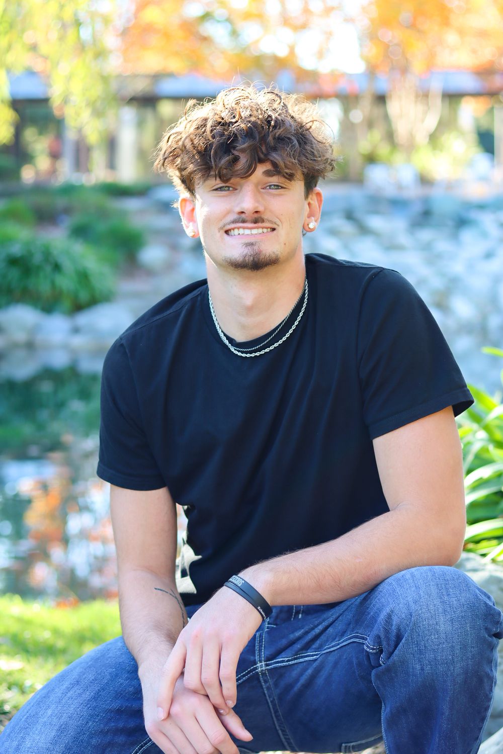Casual portrait series of person in black t-shirt and jeans sitting outdoors.