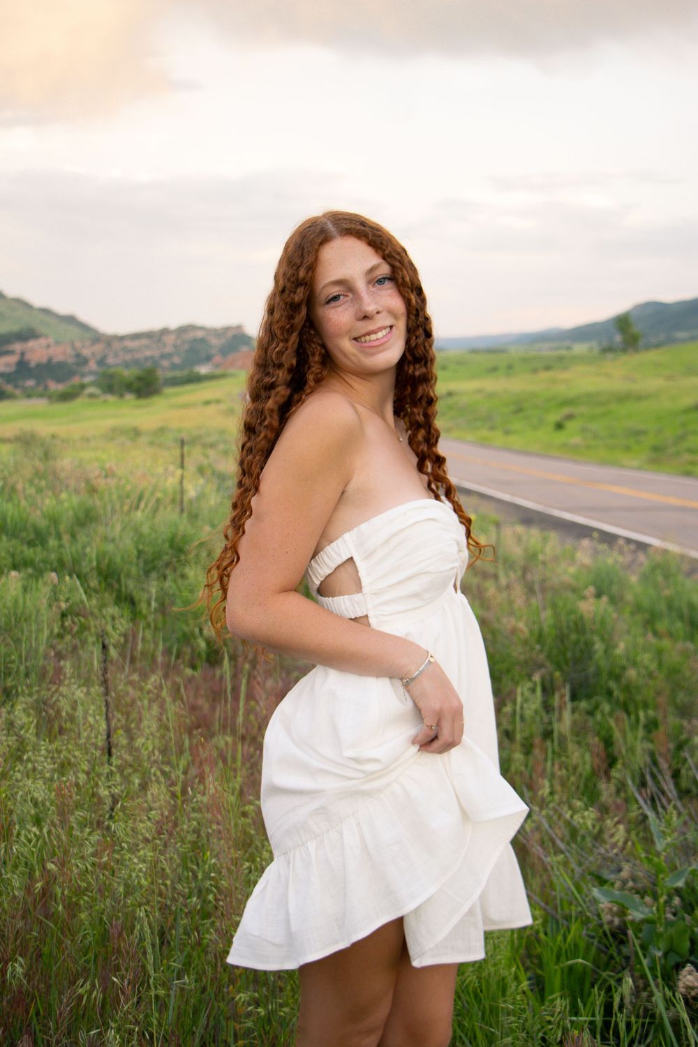 Outdoor portraits in white dress along rural road with mountains in background.