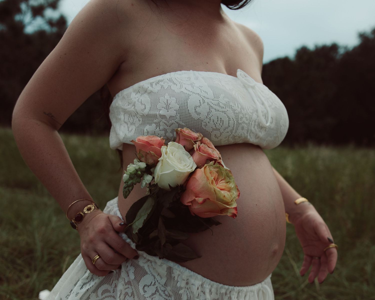 Expectant couple in casual clothes standing together against white wall, with pregnant belly visible in profile view.