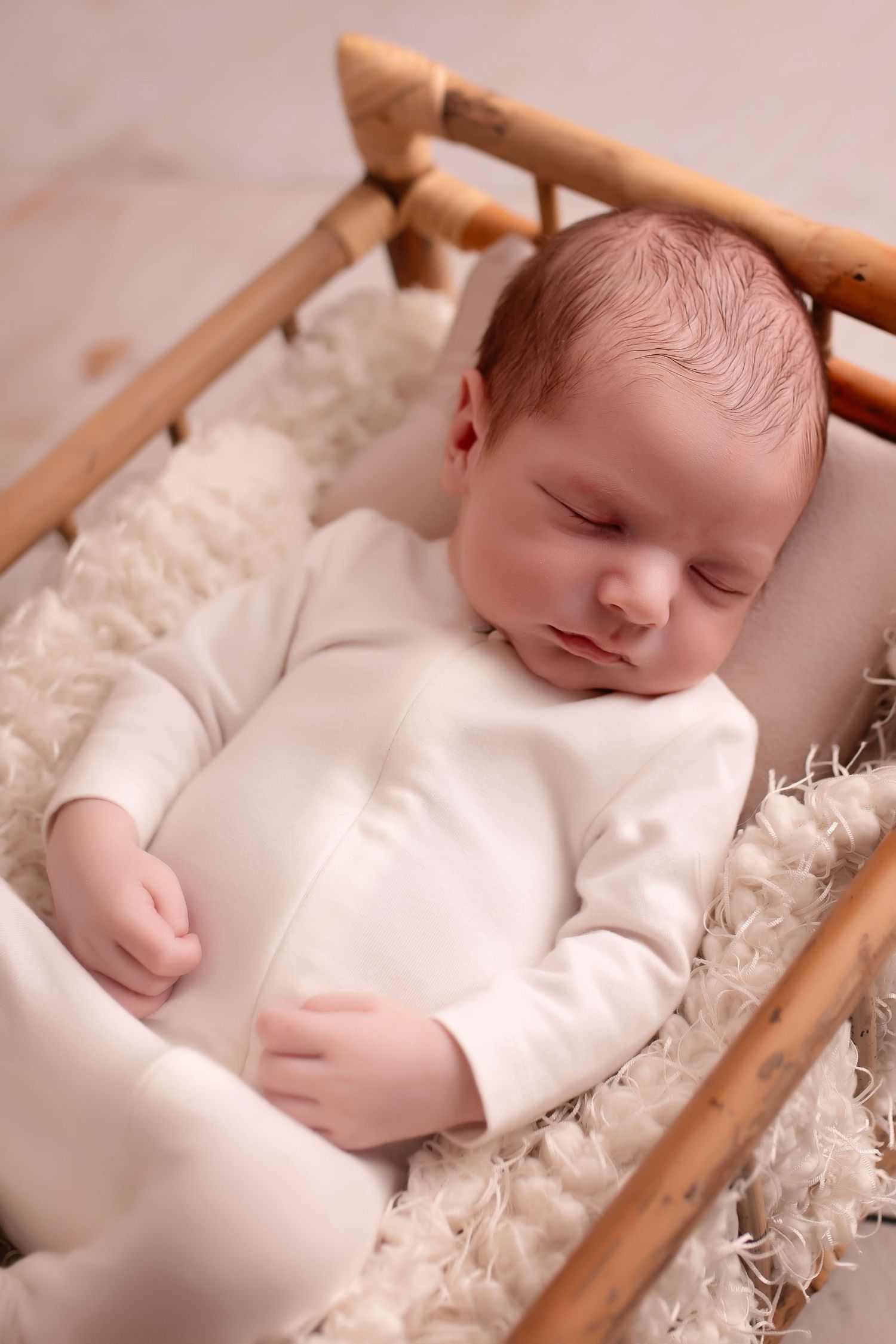Sleeping newborn in white sleeper rests peacefully in wooden basket on soft blanket.