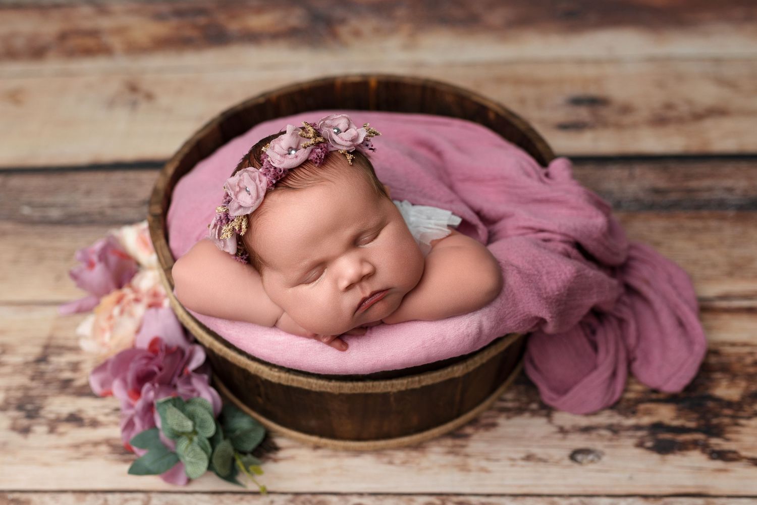 Sleeping newborn in gray knit outfit nestled in cream basket on wooden floor.