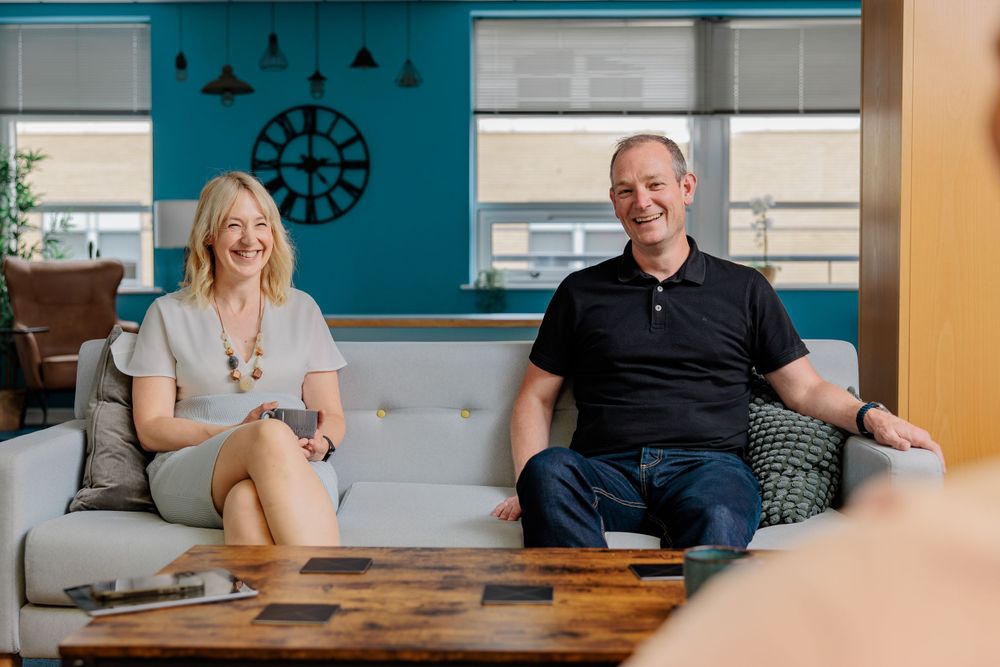 Two colleagues relax on blue couch during casual office meeting.