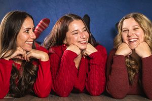 A group of people wearing red sweaters lean against each other in a row while laughing.