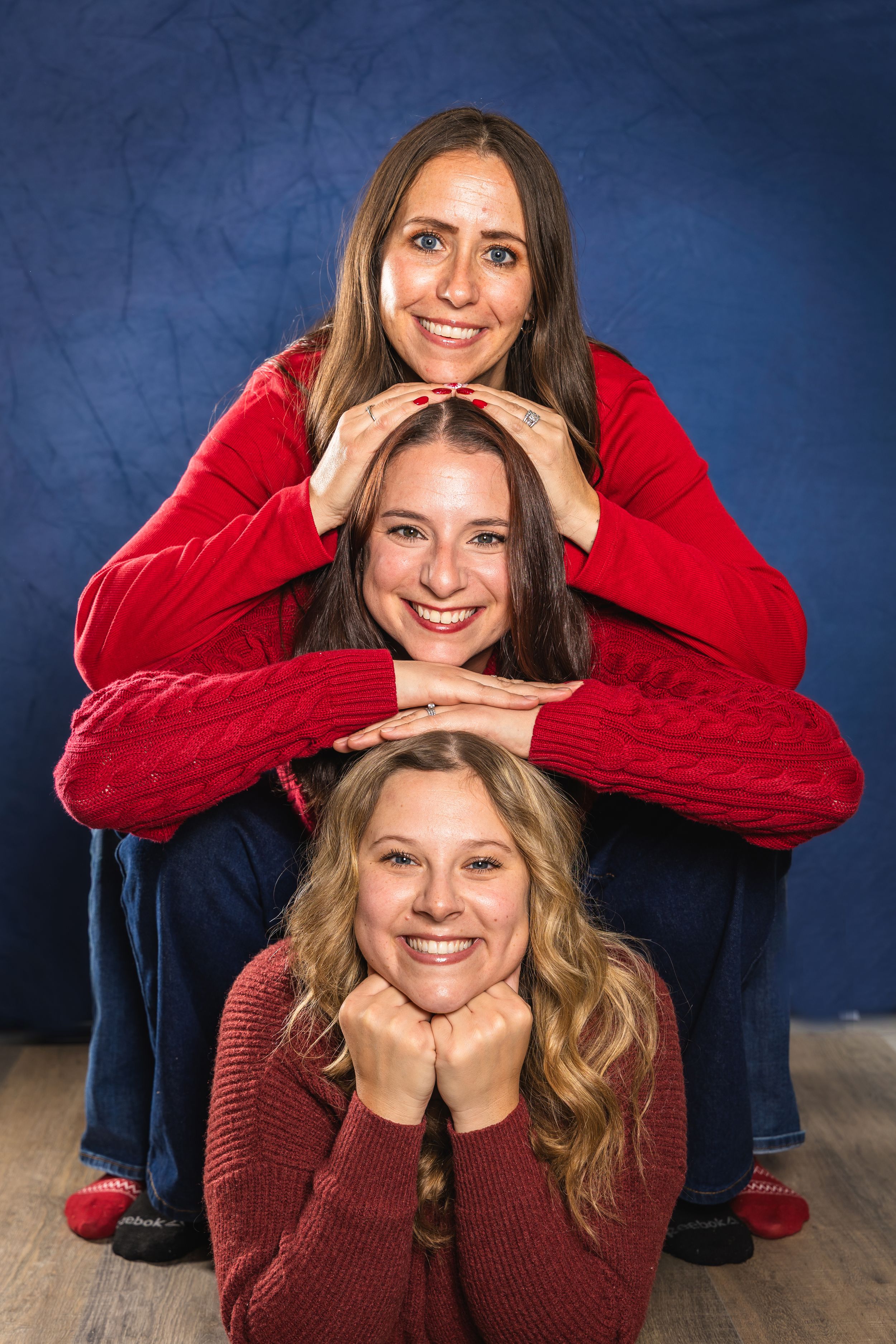 Two people in red and burgundy sweaters pose playfully for a series of casual portrait photos against a blue background.