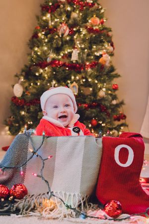 A progression of photos showing a baby peeking out from behind holiday stockings in front of a Christmas tree.
