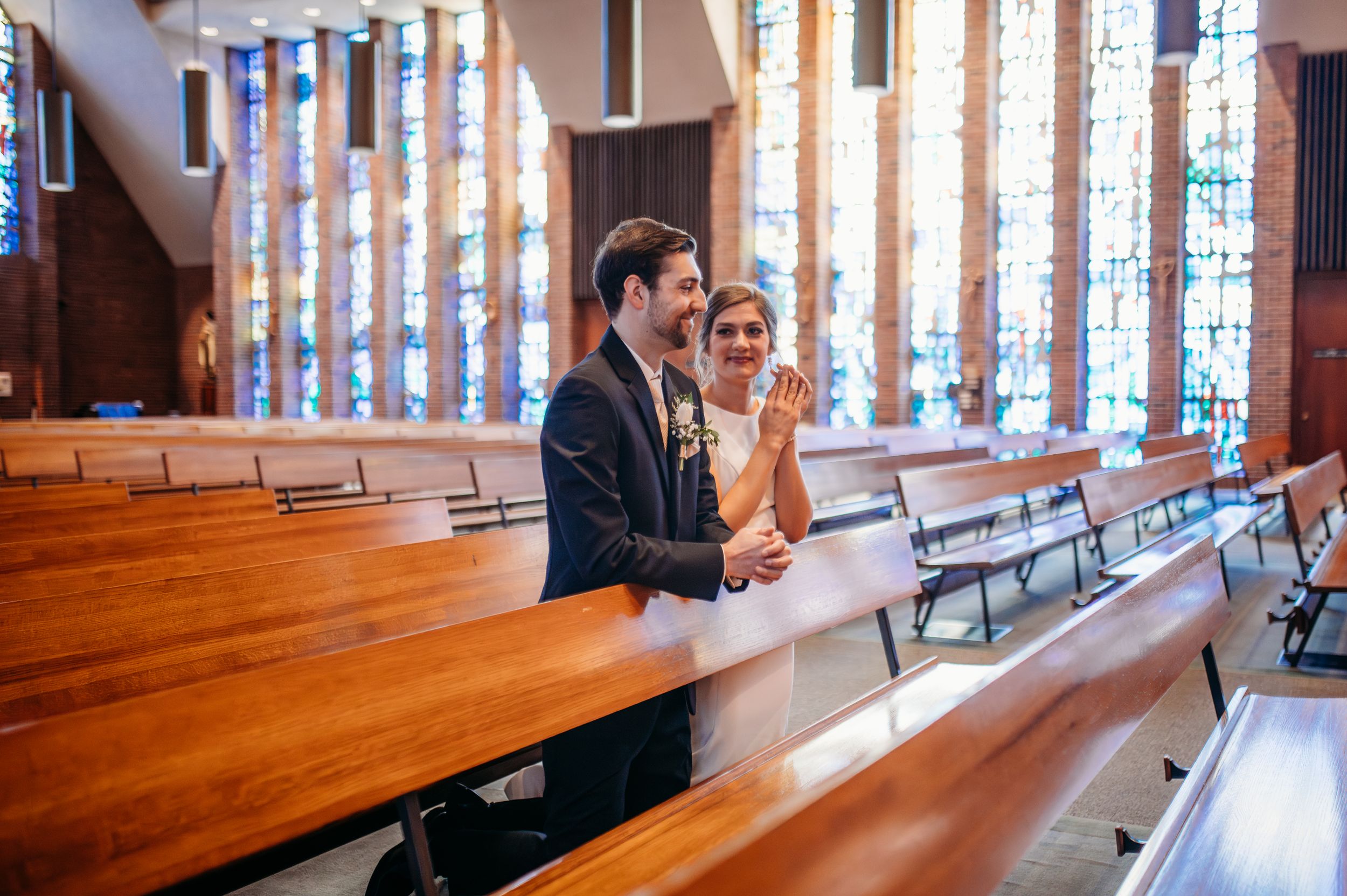 A bride glances over at her groom as they kneel together and pray in a Catholic church before their nuptial Mass.