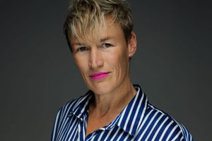 Professional portrait with dramatic lighting showing person in striped shirt against dark background.