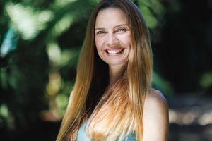 Close up portrait of a woman with long blonde hair smiling outdoors with bokeh background.