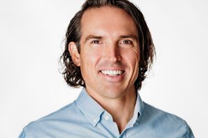 Professional headshot of man in light blue button-down shirt against white background.