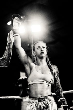 Black and white photo of a victorious boxer raising a championship belt in triumph after a match.