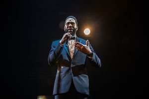 Ndaba Mandela in formal suit singing on stage with dramatic lighting.