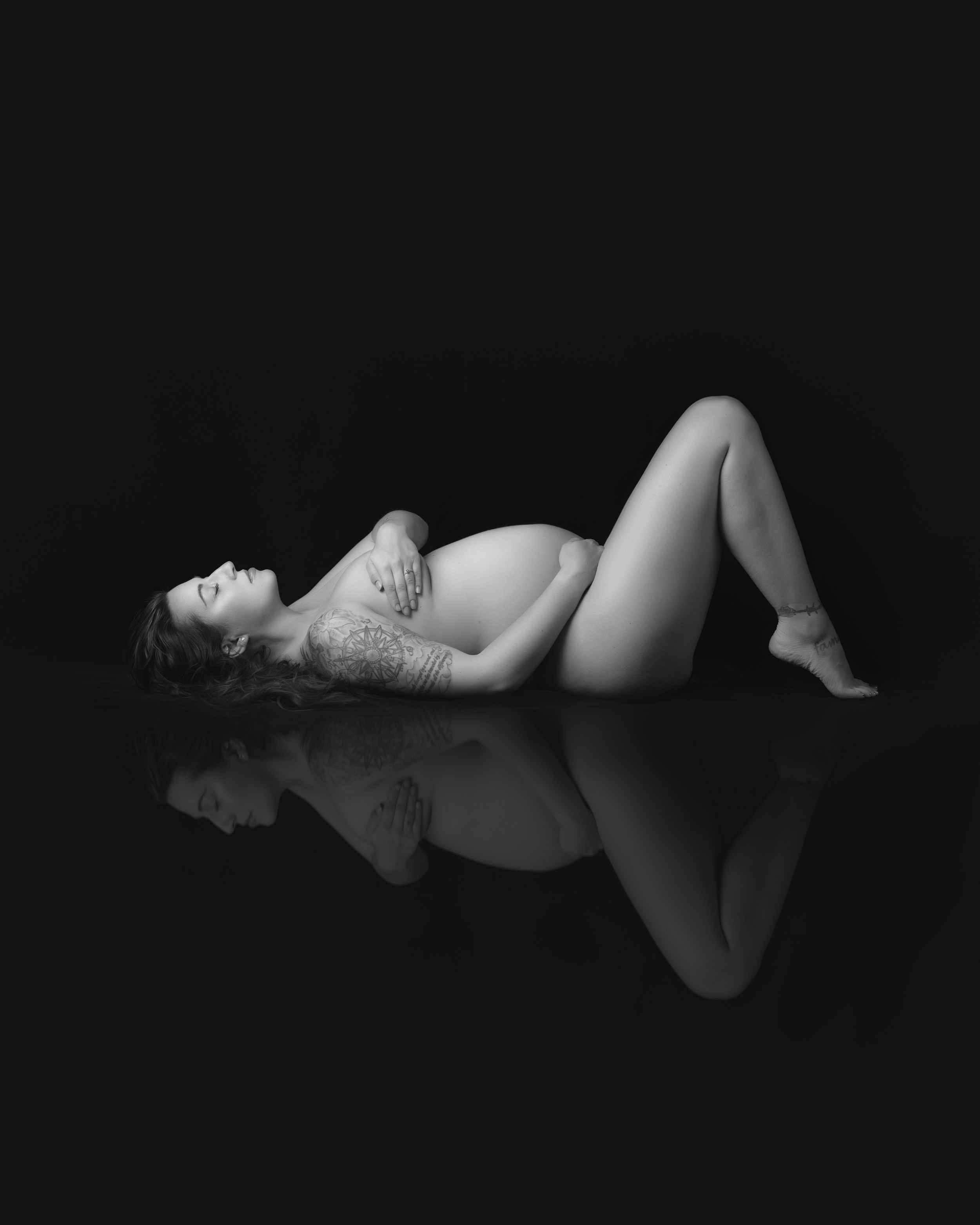 Artistic black and white maternity nude figure study with dramatic lighting and reflection.