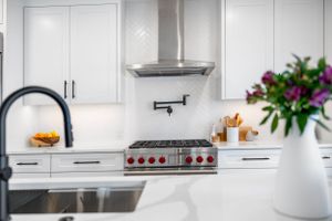 Modern white kitchen with stainless steel gas range, quartz countertops, and purple floral arrangement on display.