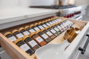An organized spice drawer with labeled jars arranged in wooden slots, showing neat rows of cooking seasonings.