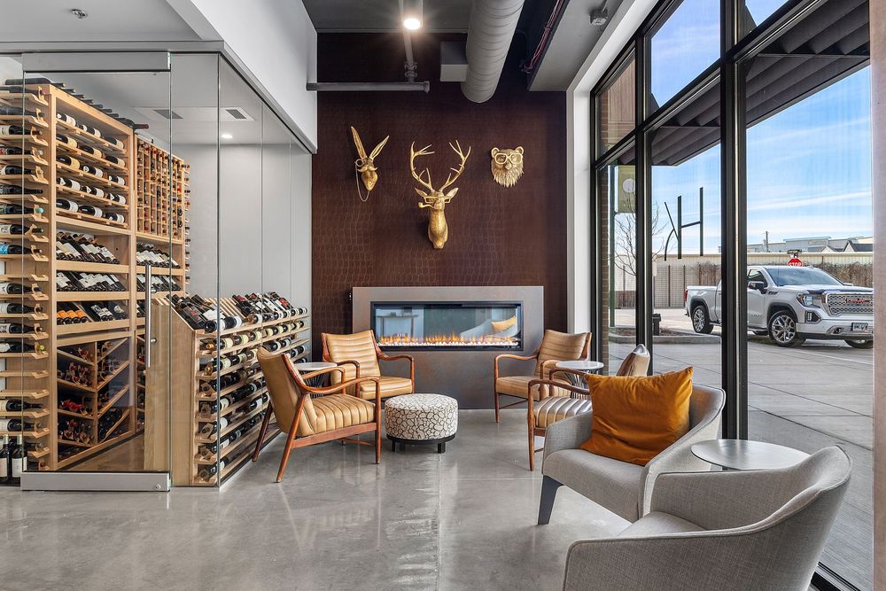 Elegant wine cellar lounge with floor-to-ceiling racks, modern fireplace, and stylish seating area featuring a gold deer head mount.