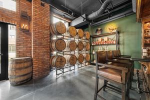 Rustic distillery tasting room with stacked bourbon barrels on brick wall, green accent wall, and wooden bar seating.