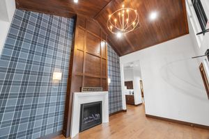 Living room with plaid accent wall, white fireplace, wood-paneled ceiling, chandelier, and hardwood floors.