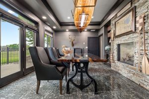 Luxurious dining room with stone fireplace, modern lighting, and elegant dark furniture.