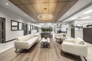 Modern office lobby with white sofas, wood ceiling accents, circular pendant light, and sleek reception desk on hardwood floors.