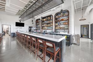 Modern bar with long white countertop, wood barstools, and backlit shelves stocked with spirits.