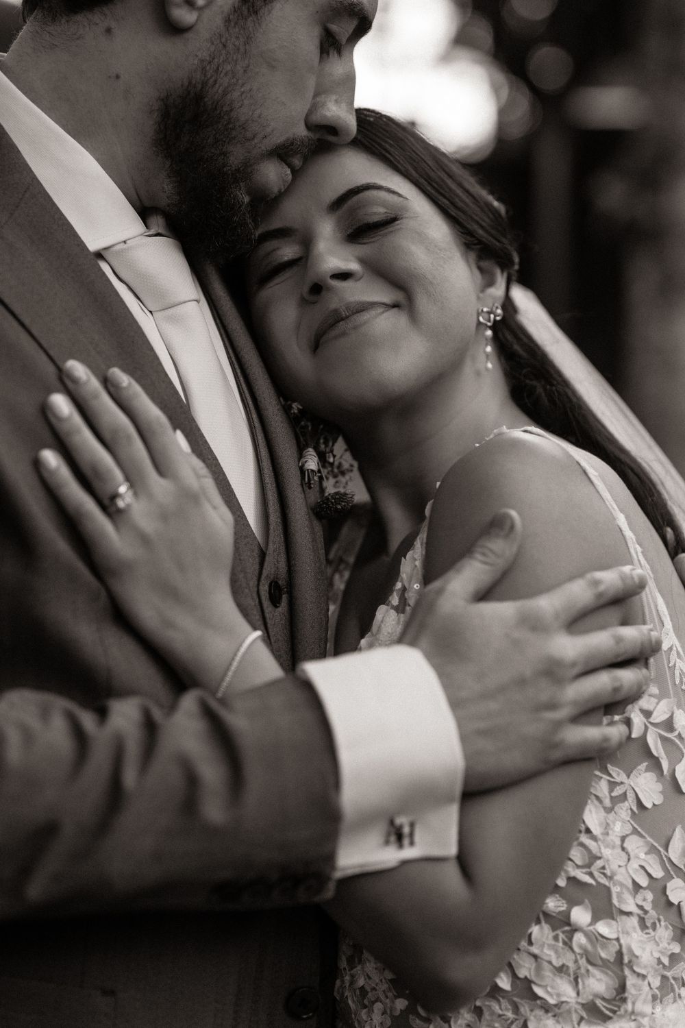 Black and white photo of a bride and groom embracing tenderly, the groom kissing her forehead as she smiles peacefully.