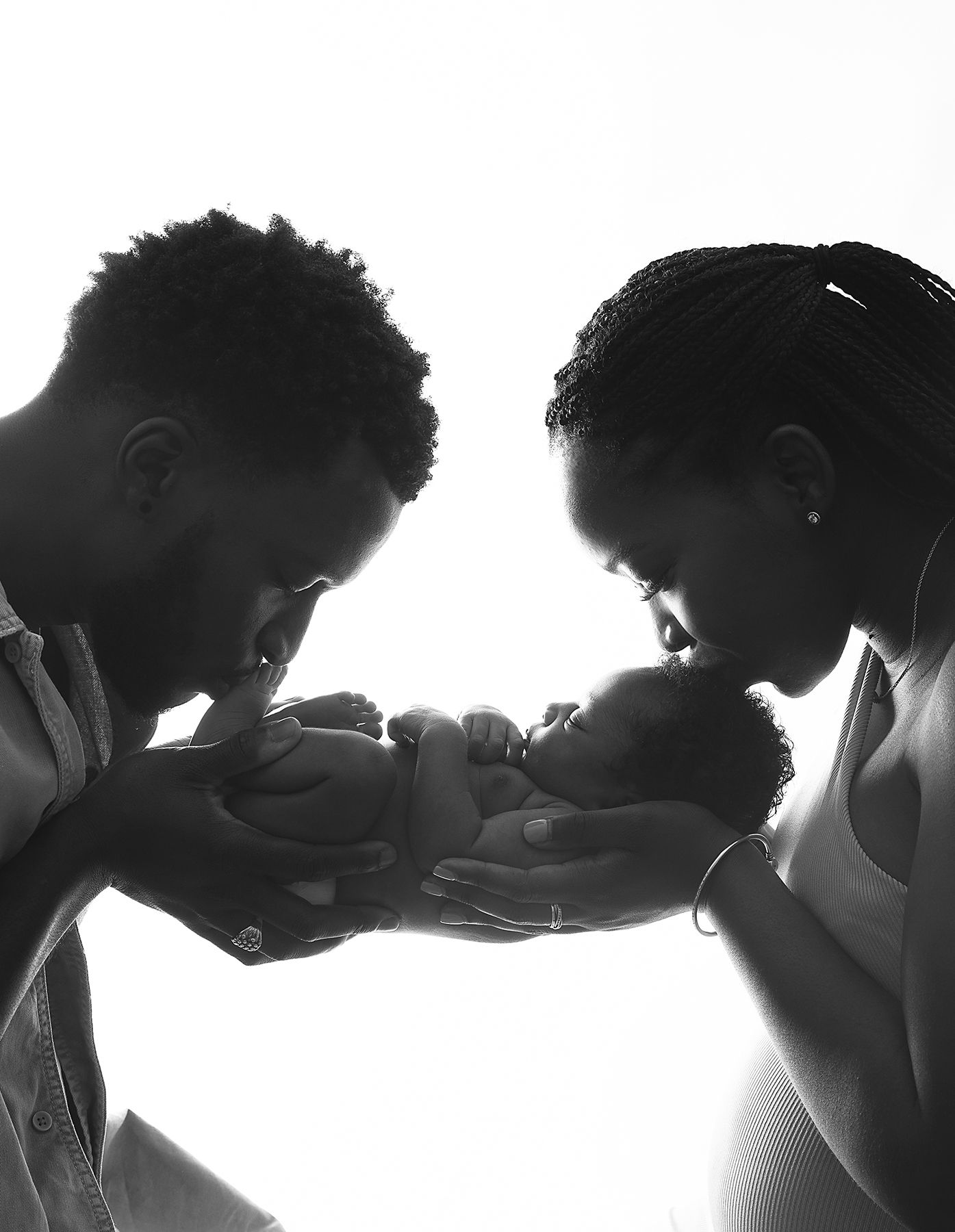 Black and white silhouette photo of parents lovingly cradling their newborn baby together in tender moment. During a newborn shoot in London