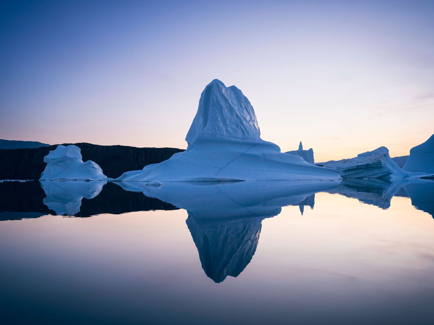 Icebergs reflected in calm waters during twilight creating perfect mirror images.