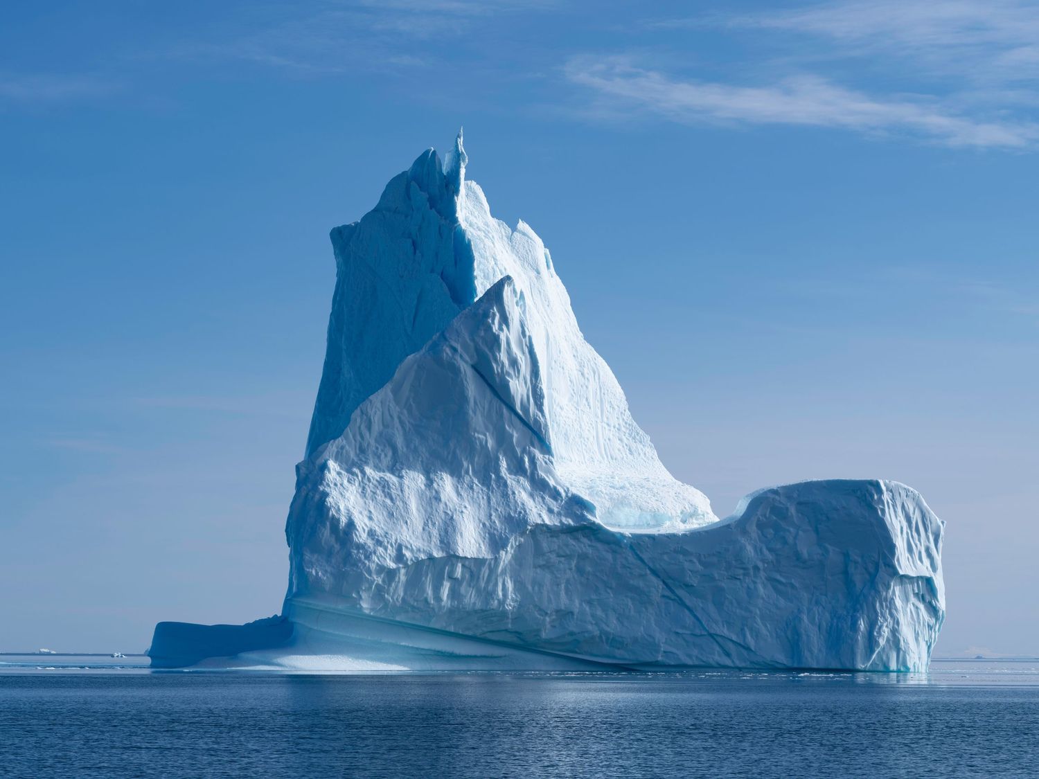 Majestic white iceberg towers above the ocean under bright blue skies.
