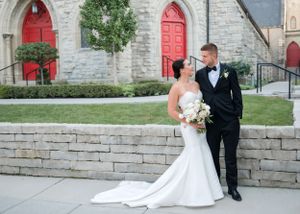 A bride and groom pose outside a stone church with red doors.