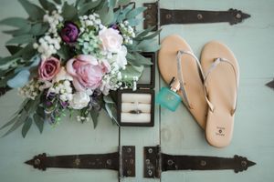 Wedding details including flowers, sandals and ring box arranged on turquoise surface.