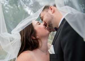 Romantic wedding photo of a couple sharing a kiss under a flowing veil.