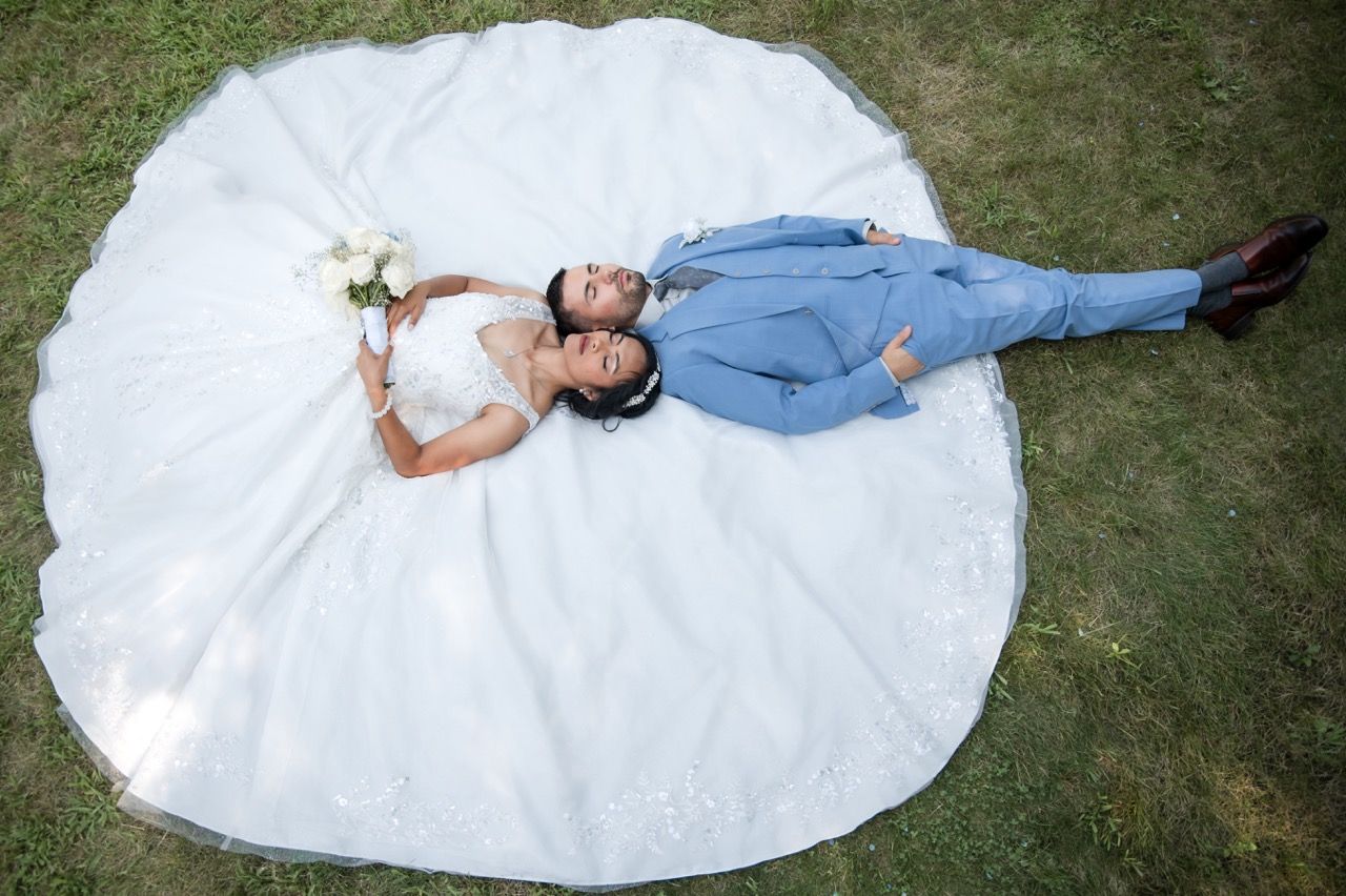 Aerial view of newlyweds lying on grass with bride's dress spread in perfect circle.