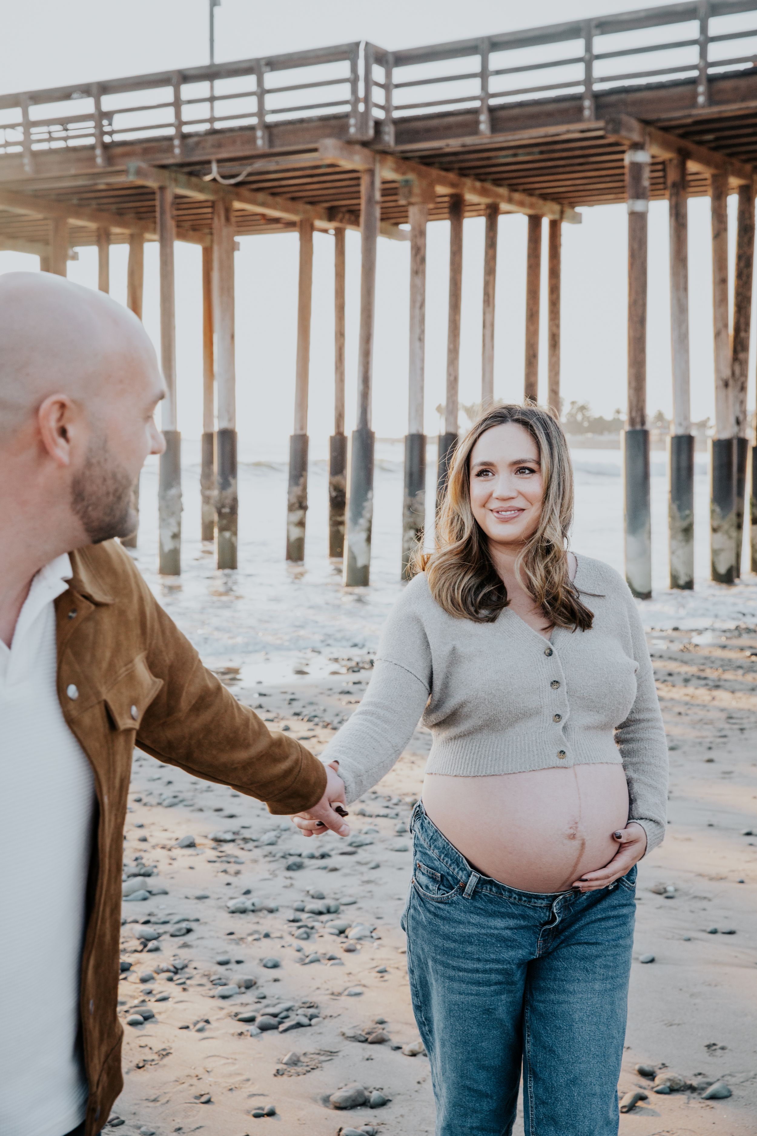 Maternity photoshoot on beach with pier in background during golden hour.
