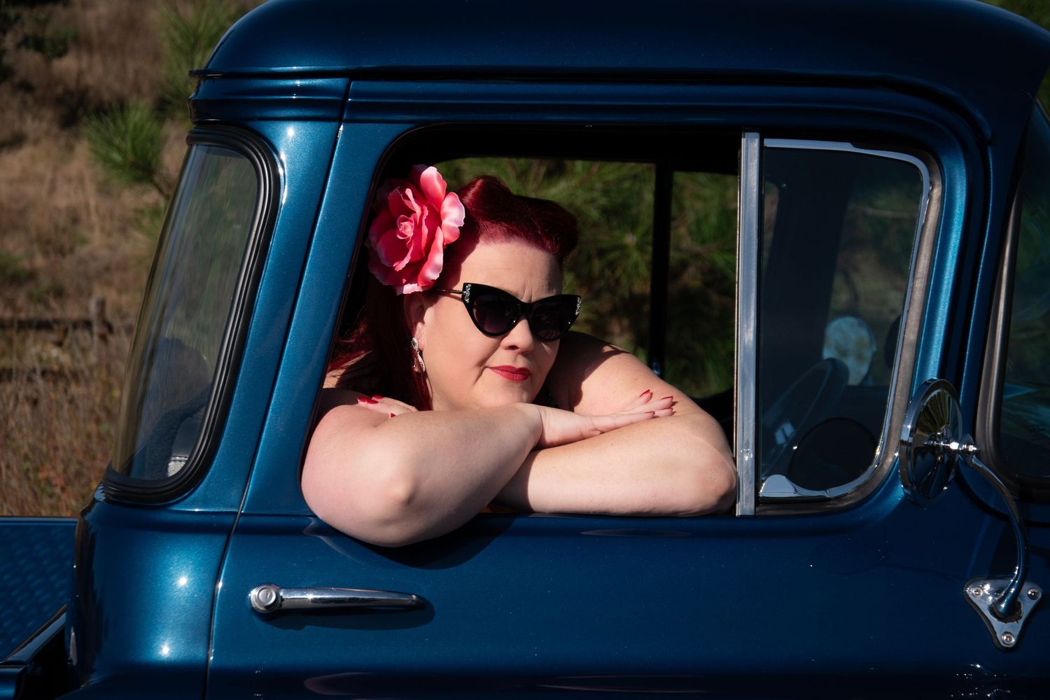 Person wearing sunglasses poses in vintage blue truck with retro styling.