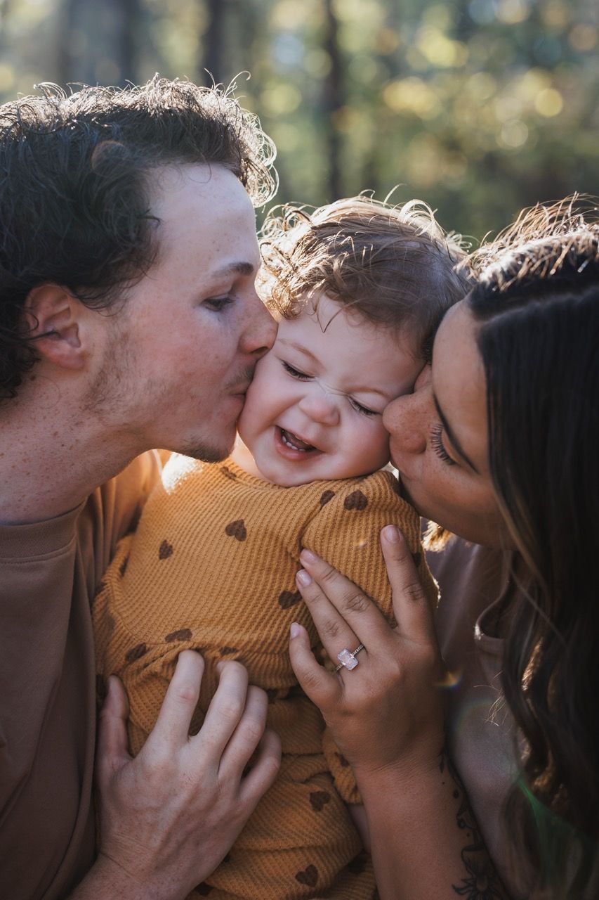 Intimate moment of parents kissing toddler in a Snohomish woodland. Warm and raw family storytelling by Tim Neal.