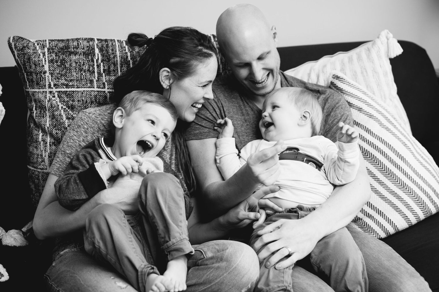 Candid black and white family moments captured on a cozy couch showing genuine laughter and joy.