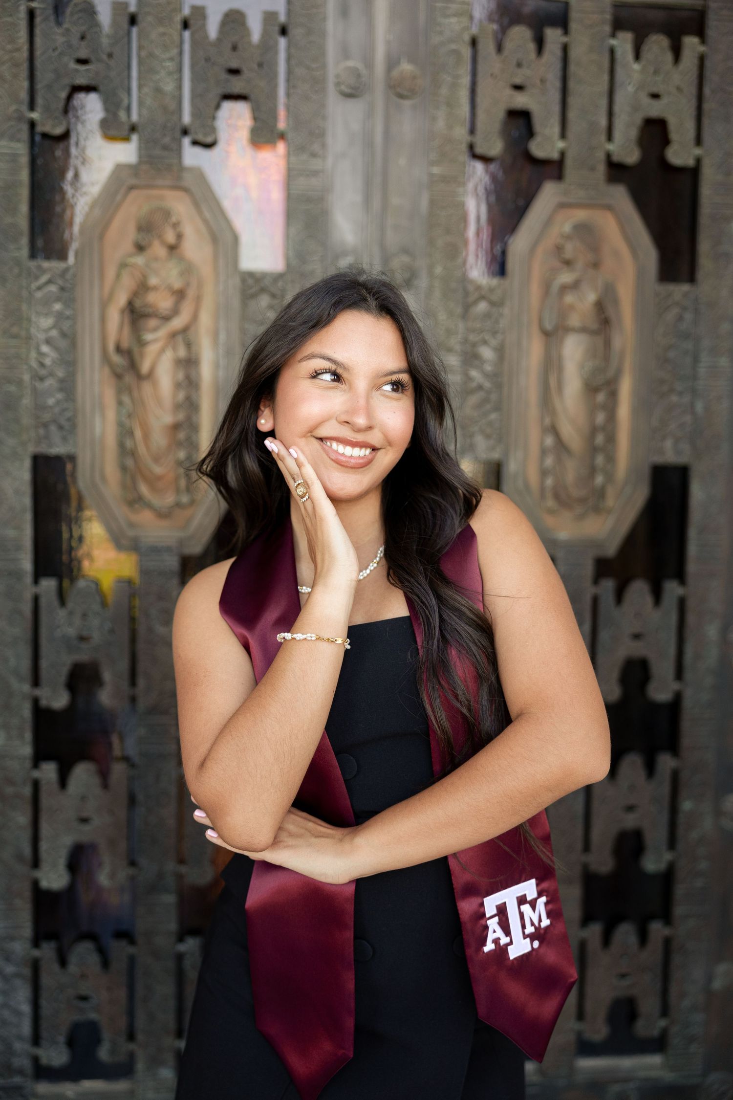 A figure in a black dress with light blue sash poses in front of an ornate architectural doorway.