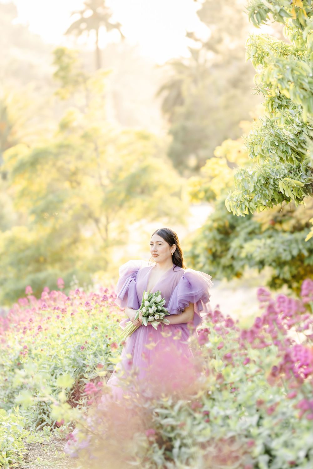 A dreamy garden portrait with someone in a purple dress among pink wildflowers at golden hour.